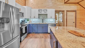 Una cocina moderna con electrodomésticos de acero inoxidable, armarios azules y techo de madera.