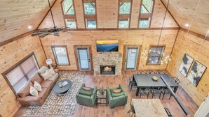 Una cabaña espaciosa con techos altos, chimenea, comedor y zona de estar con sofá y sillones.