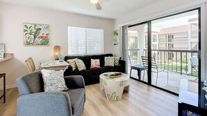 Ein modernes Wohnzimmer mit einer schwarzen Couch, einem grauen Sessel, einem kleinen runden Tisch und einem Deckenventilator.