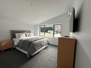 A bedroom with a bed, a nightstand, a dresser, a window, and a TV.