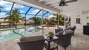Un espacio al aire libre techado con piscina, muebles de mimbre y ventilador de techo.
