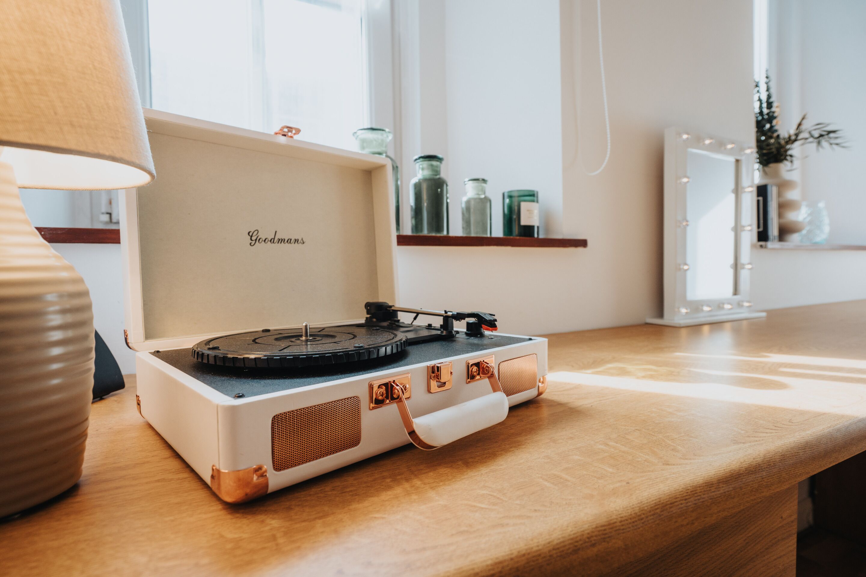 A turntable on a wooden table with a lamp, a mirror with lights, and shelves with glass jars.