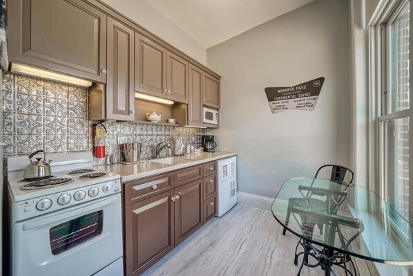 A kitchen with a stove, microwave, and cabinets. There is a glass table with chairs and a sign on the wall. - Downtown ~ Near River & Trails ~ Palace Hotel (Salida)