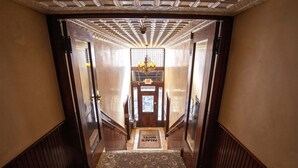 A hotel lobby with a carpeted staircase, wooden doors, a chandelier, and a sign reading 'EXIT' above the door. - Downtown ~ Near River & Trails ~ Palace Hotel (Salida)