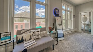 A hotel room with large windows, a sofa with decorative pillows, a small table with a clock, and a large mirror. - Downtown ~ Near River & Trails ~ Palace Hotel (Salida)
