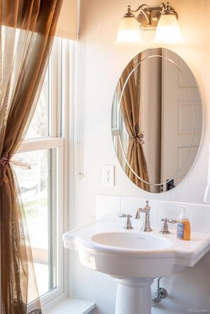 A bathroom with a white sink, a round mirror, and a light fixture above the mirror. - Downtown ~ Near River & Trails ~ Palace Hotel (Salida)