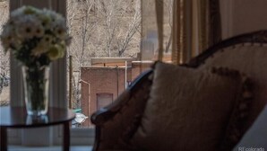 A room with a large window overlooking a hill with a sign. There is a vase with flowers on a table in the foreground. - Downtown ~ Near River & Trails ~ Palace Hotel (Salida)