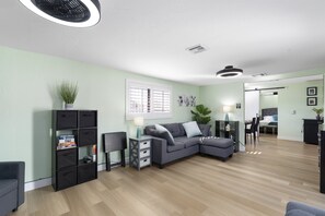 Un salon moderne avec un canapé d’angle gris, une bibliothèque noire et une petite table d’appoint avec une lampe.