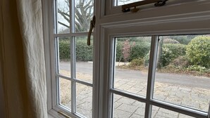 Une fenêtre donnant sur une zone pavée et sur de la verdure à l’extérieur.