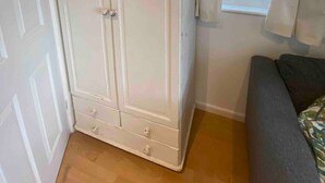 Une pièce avec une grande armoire blanche, une fenêtre avec des rideaux et un canapé gris.