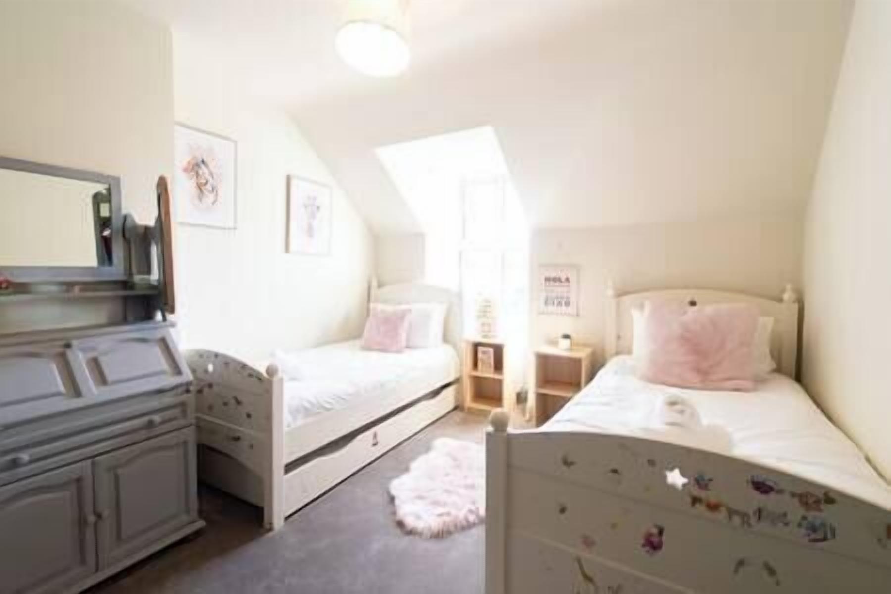 Een slaapkamer met twee eenpersoonsbedden, een dressoir, een spiegel en een klein bureau.