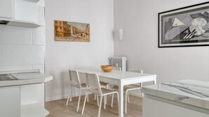 A modern kitchen with white cabinetry, a dining table with chairs, and two framed artworks on the walls. - Iroko Living - Turro (Milano)
