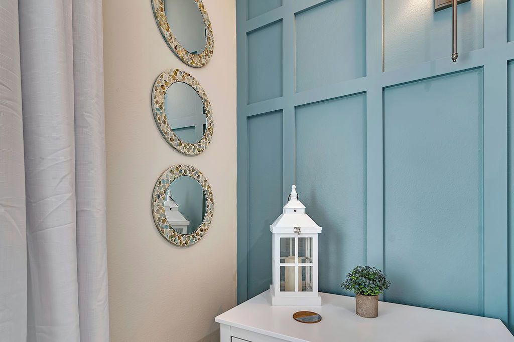 Un baño con tocador blanco, tres espejos de mosaico, un farol blanco y una planta en maceta.