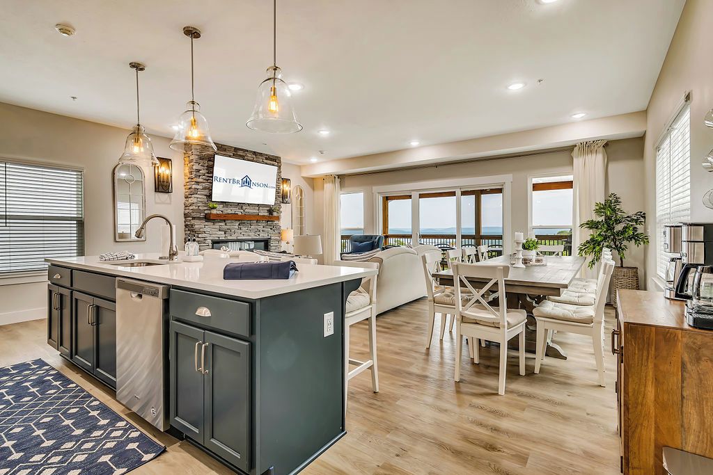 A modern kitchen with a central island, built-in appliances, pendant lighting, and a view to the outside.