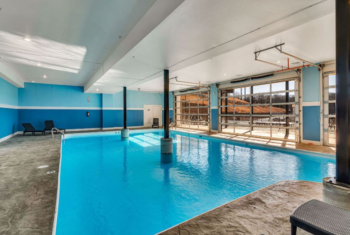 An indoor swimming pool with clear blue water, surrounded by blue walls and a large window.