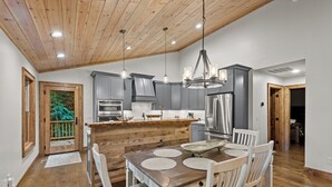 Una cocina moderna con armarios grises, electrodomésticos de acero inoxidable y una isla de madera con una mesa y sillas.
