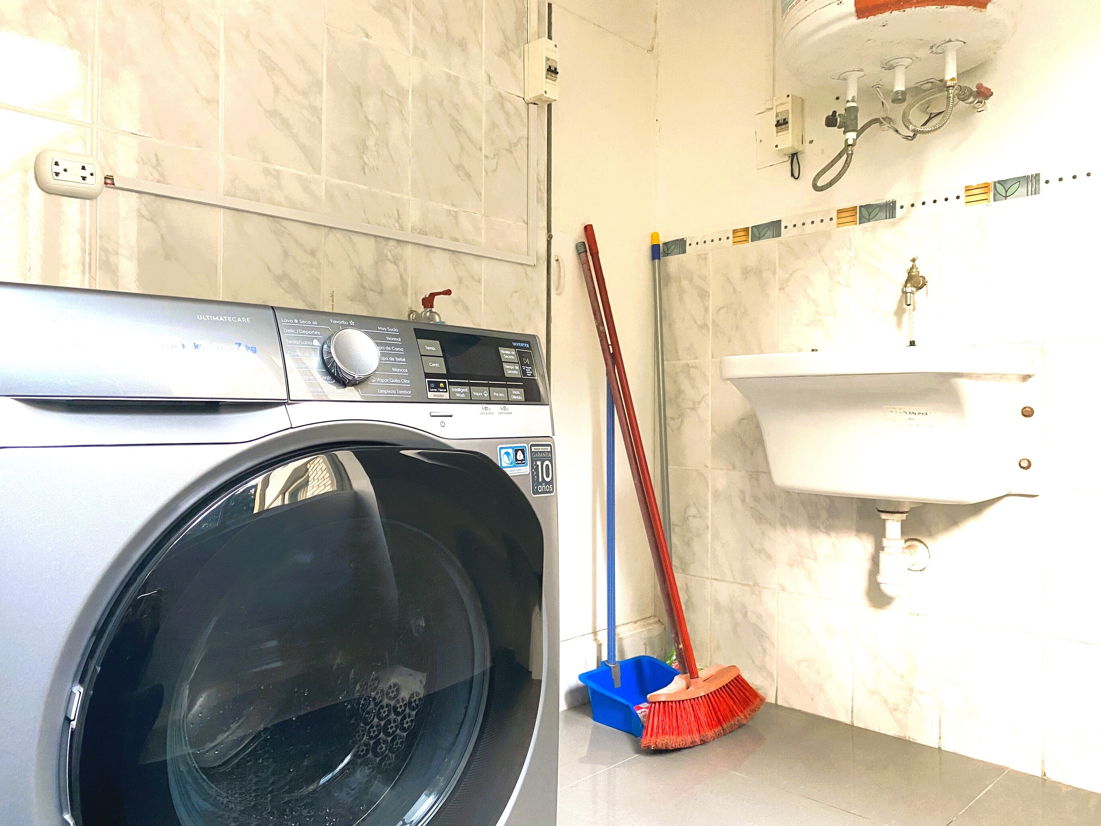 Un espace dédié à la lessive, avec un lave-linge, un panier à linge bleu et un balai rouge appuyé contre le mur.