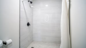A modern bathroom with a glass shower enclosure, a toilet, and a roll of toilet paper on the wall. - ERTH INN by AGA- San Ysidro (San Ysidro)