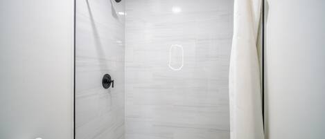 A modern bathroom with a glass shower enclosure, a toilet, and a roll of toilet paper on the wall.