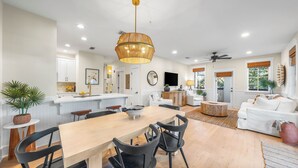 A spacious living area with a wooden dining table, black chairs, a white sofa, and a ceiling fan.