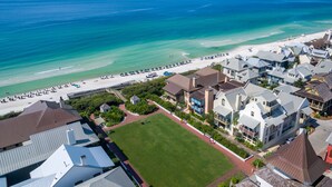 An aerial view of a coastal town with a beach, houses, and a large green lawn.