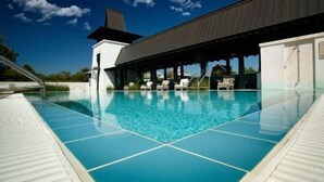 A swimming pool with clear blue water, a covered seating area, and a white building with a dark roof.