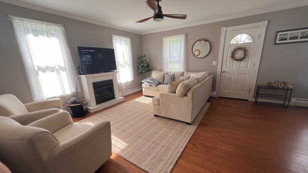 A living room with a fireplace, a television, a sofa, and a ceiling fan. - The Red House  (Sodus Point)