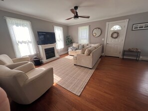 A living room with a fireplace, a television, a sofa, and a ceiling fan. - The Red House  (Sodus Point)