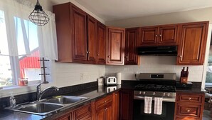 A kitchen with wooden cabinets, a stainless steel sink, a toaster, and a stove. - The Red House  (Sodus Point)