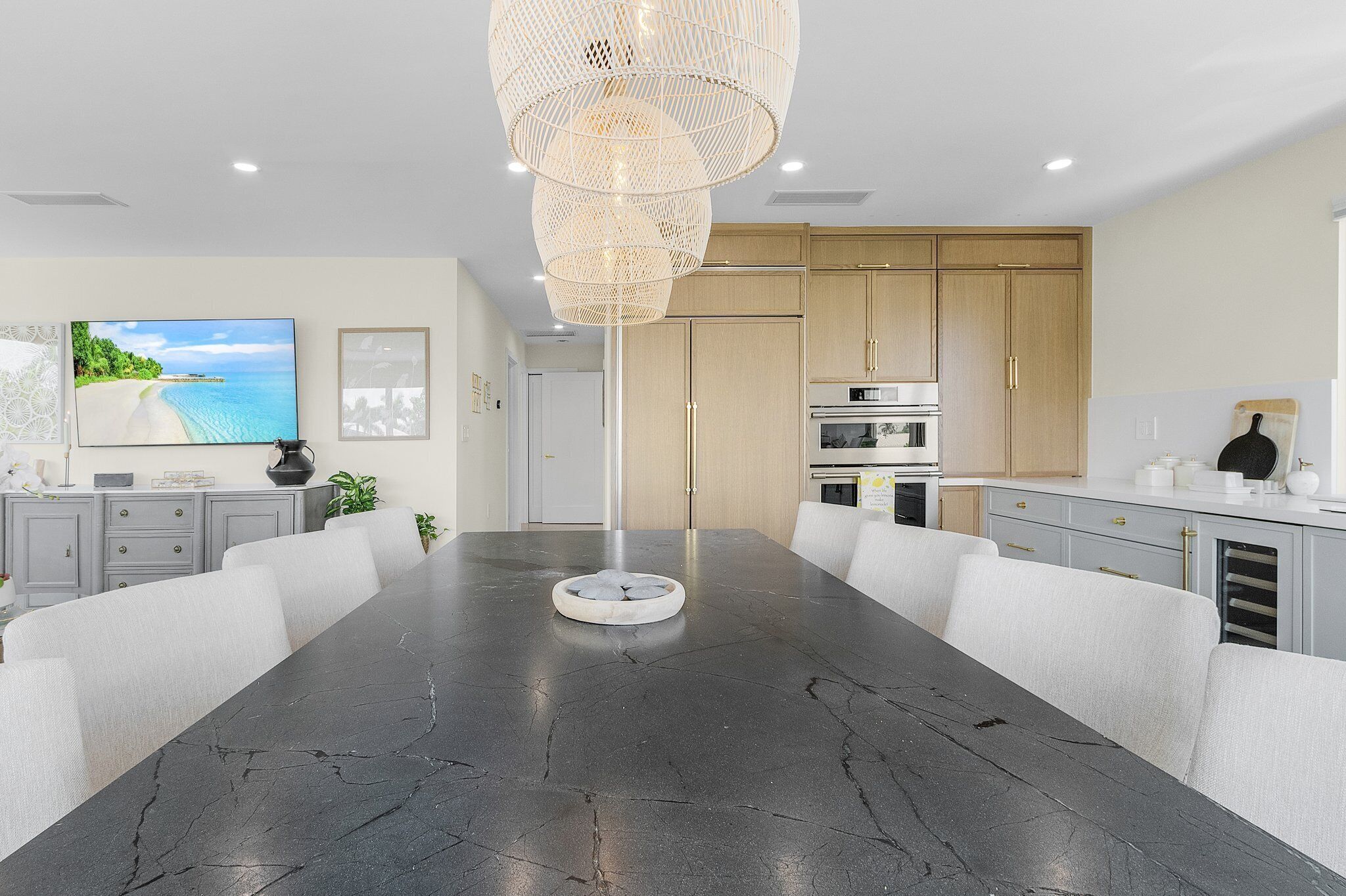 A modern kitchen with wooden cabinets, a large island, and a dining area with a marble table.