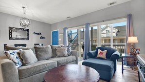 A living room with a grey sofa, a blue armchair, a round coffee table, a chandelier, a mirror, and a sign that reads "Beach Sea".