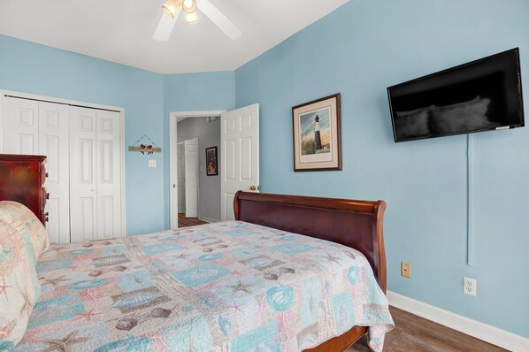 A bedroom with a bed, a television mounted on the wall, and a door leading to another room.