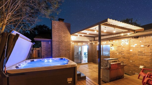 An outdoor patio with a hot tub, barbecue grill, and string lights. - 3 bed home with Luxury Hot Tub, Deck, Wifi and Arcade Games  (Houston)