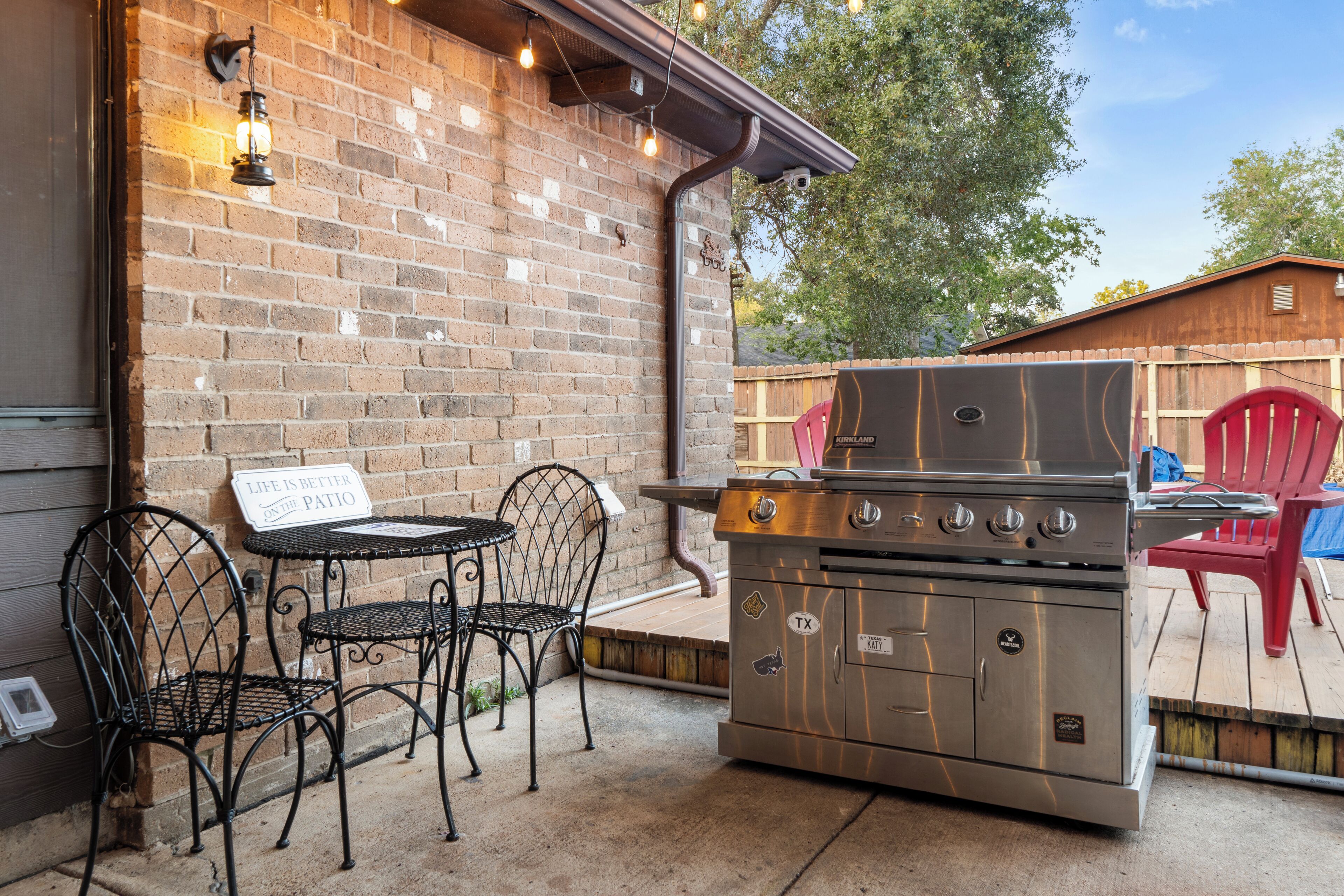 An outdoor patio with a brick wall, metal chairs, a table, and a stainless steel grill.