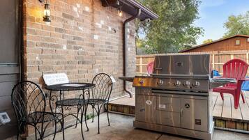 An outdoor patio with a brick wall, metal chairs, a table, and a stainless steel grill.