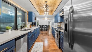 A modern kitchen with stainless steel appliances, blue cabinets, and a wooden ceiling. - 3 bed home with Luxury Hot Tub, Deck, Wifi and Arcade Games  (Houston)