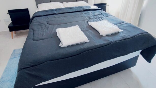 A modern bedroom with a large bed, grey headboard, white pillows, and a blue accent pillow.