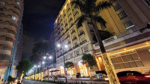 A multi-story hotel with balconies, a street with palm trees, and illuminated decorations. - 101 Newport Blvd: SkyStag Aerie - A cozy studio near NAIA Terminal 3 Airport (Pasay)