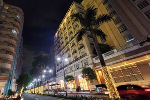 Un hôtel à plusieurs étages doté de balcons, une rue bordée de palmiers et des décorations illuminées.