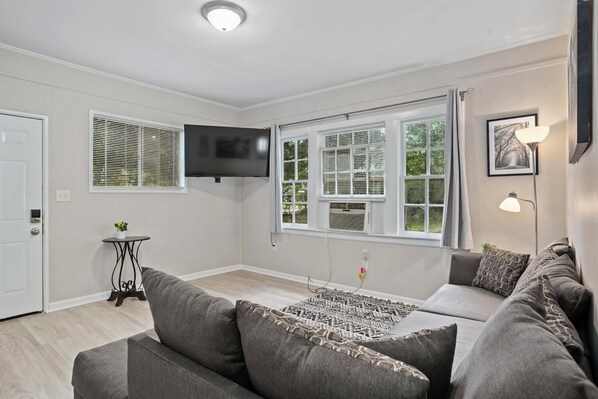 A living room with a grey sofa, a small table, and a TV mounted on the wall.