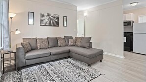 Un salon moderne avec un canapé d’angle gris, un tapis à motifs et une décoration minimaliste.