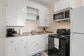 A compact kitchen with white cabinets, a black stove, a microwave, and a coffee maker.