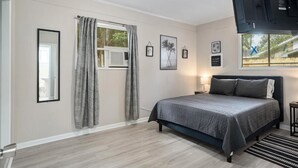 Une chambre à coucher avec un lit, une fenêtre avec des rideaux, une table de chevet avec une lampe et des tableaux encadrés accrochés au mur.