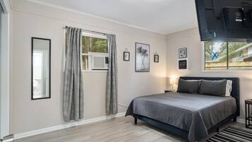 Une chambre à coucher avec un lit, une fenêtre avec des rideaux, une table de chevet avec une lampe et des tableaux encadrés accrochés au mur.