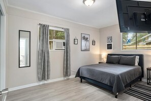 A bedroom with a bed, a window with curtains, a bedside table with a lamp, and framed pictures on the wall.