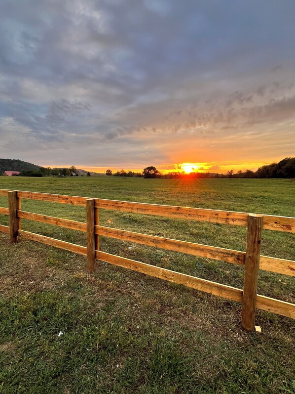 A wooden fence in a grassy field with a sunset in the background.