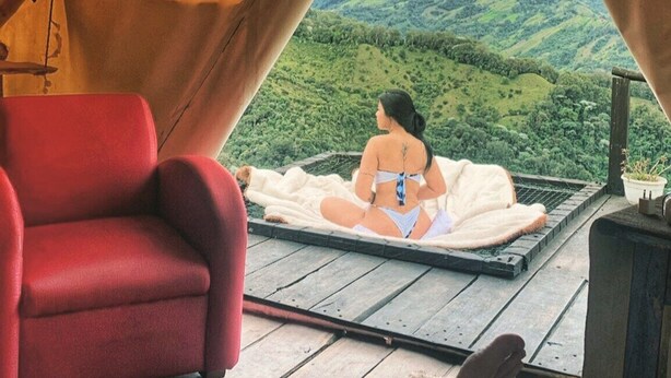 A tent with a view of green hills, a red chair, and a person sitting on a blanket. - Glamping Rustiko Salento  (Salento)