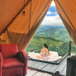 A tent with a view of green hills, a red chair, and a person sitting on a blanket. - Glamping Rustiko Salento  (Salento)