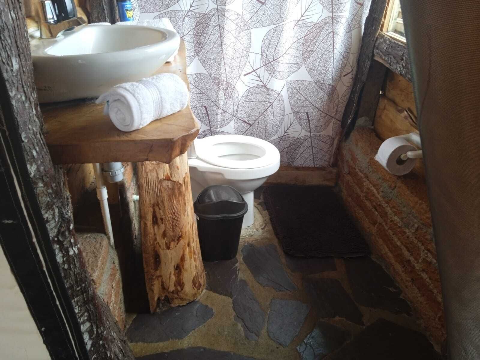 Une salle de bain rustique avec un sol en pierre, un lavabo en bois, des toilettes et une poubelle noire.
