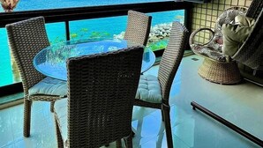 A balcony with wicker chairs, a glass table, and a view of the ocean. - Apt Luxo ao lado da Praia no Porto Real  (Mangaratiba)